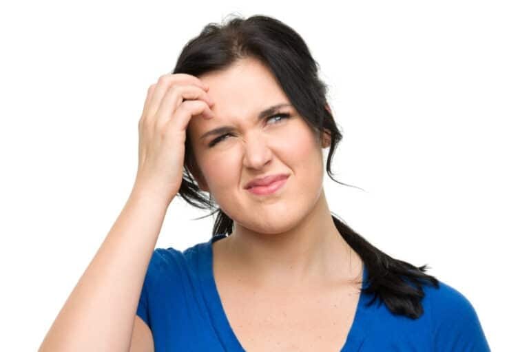 Woman with dark hair and blue t-shirt looking confused and scratching her head.